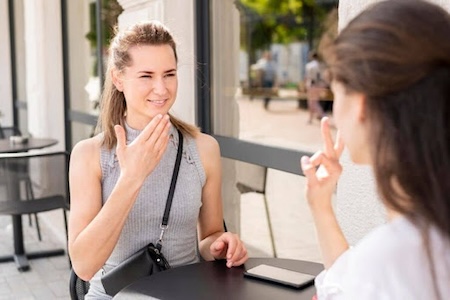 Two girls sitting beside a table and sign language.