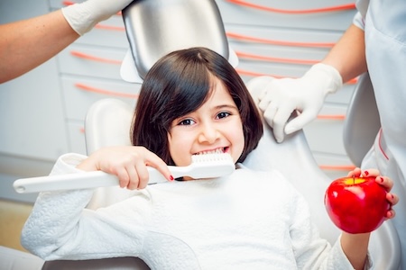 An adorable child at the dentist's office brushing and holding an apple.
