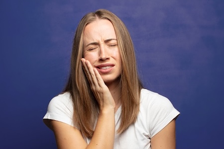 A girl is holding her cheek because of wisdom tooth pain.