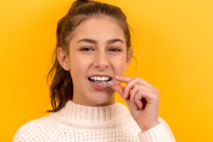 Woman using clear dental aligner, yellow background